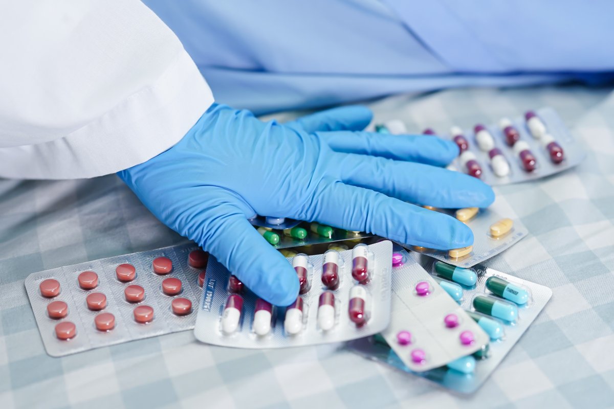 Hånd med plasthanske holder over ulike brett med antibiotikum.