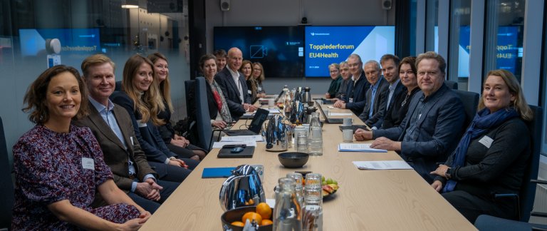 Personer sitter rundt et langbord i et møtelokale.