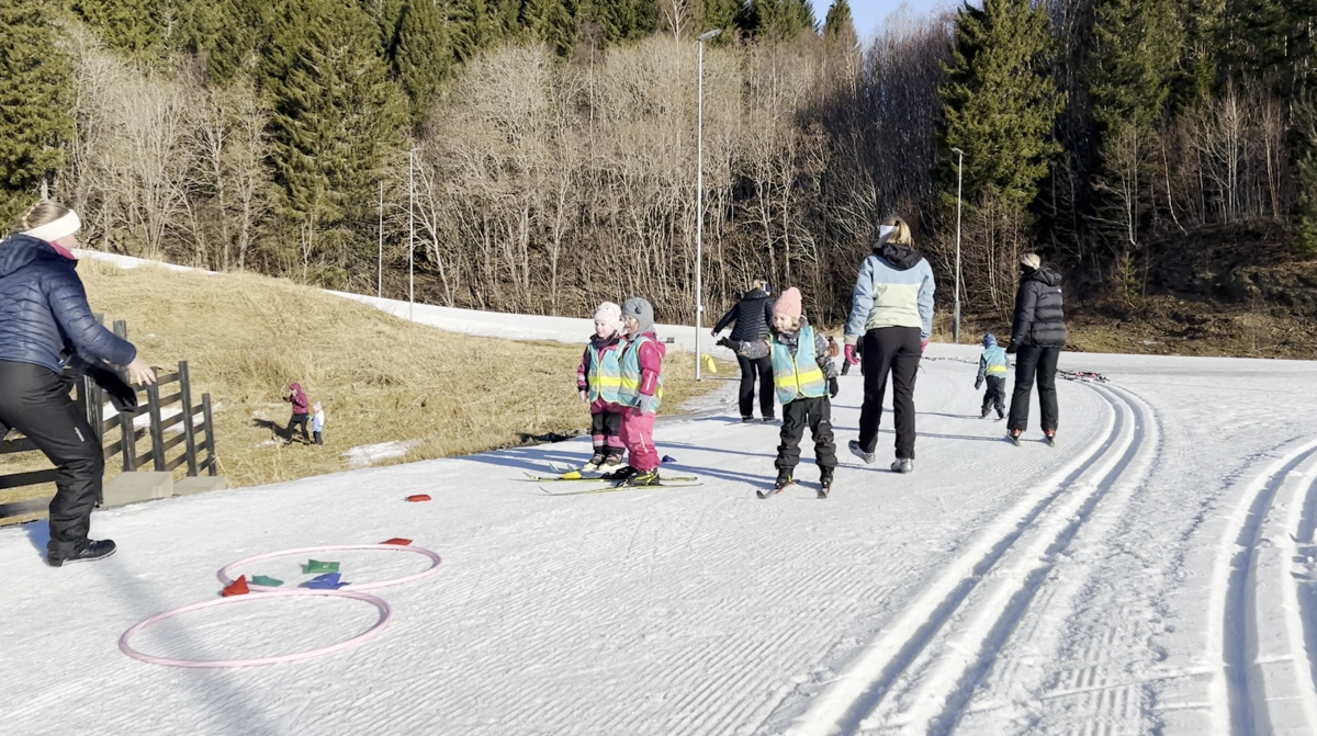 Barn med langrennski og voksne i skiløype  
