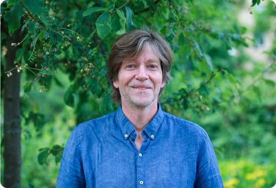 Smilende mann i blå skjorte omringet av natur